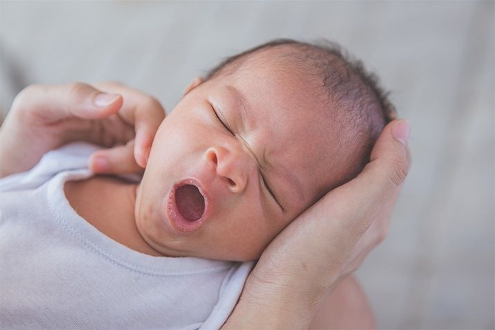 Nyfödd bebis gäspar medan den hålls varsamt i vuxnas händer